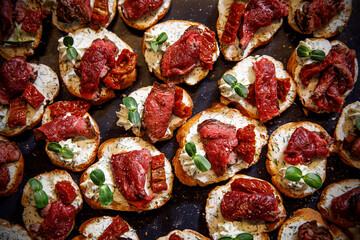 Meat bruschetta on a black tray. Beef and dried tomato on a baguette.