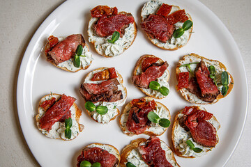Meat bruschetta on a black tray. Beef and dried tomato on a baguette.