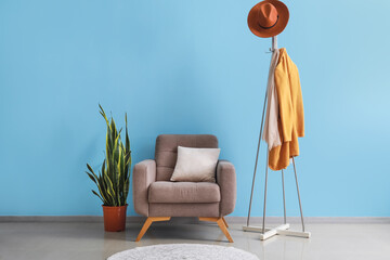 Interior of room with armchair, houseplant and rack near color wall