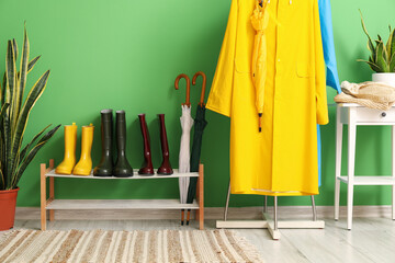 Rack with raincoats and shoes stand near green wall