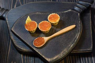 Tartlets with red caviar on a wooden cutting board. Close-up, selective focus.