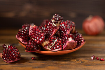 Cut fruits of ripe pomegranate in a clay bowl on a wooden table. Close-up. Selective focus.