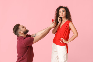 Young man proposing to his girlfriend on color background
