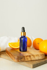 Bottle of essential oil and fresh oranges on light background