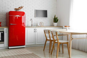 Interior of light kitchen with red fridge, white counters and dining table