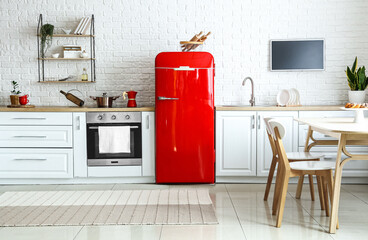 Interior of light kitchen with red fridge, white counters and dining table - obrazy, fototapety, plakaty