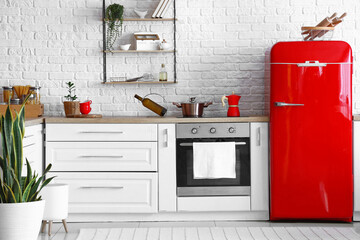 Interior of light kitchen with red fridge, white counters and oven