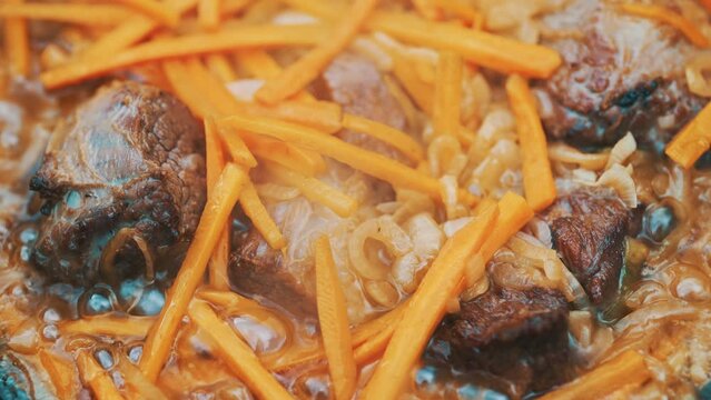 Meat and carrot is cooked in cauldron on fire.