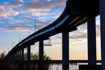Looking up at the architectural silhouette of the Highway 98 bridge in Apalachicola, Florida with a blue sky and clouds during sunrise.