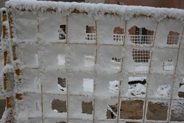 The fence grid is strewn with frost crystals, snowflakes. Winter snowy frosty background. World Snow Day