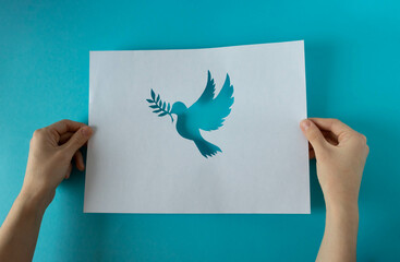 Hands holding a paper pigeon stencil on a blue background. World Peace Day. World Science Day for...