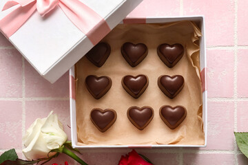 Box with tasty heart-shaped candies and flower on pink background