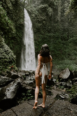 A young woman traveller is exploring a waterfall in tropical settings of Bali islands, Indonesia. Tropical forest, lush greenery, river