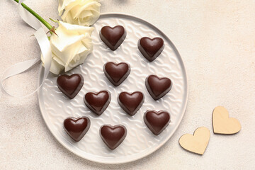 Plate with tasty heart-shaped candies and flowers on light background