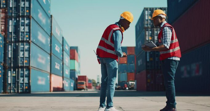 ndustrial Engineer with Tablet and Black African American Male Supervisor in Hard Hats and Safety Vests Stand in Container Terminal. Colleagues Talk About Logistics Operations