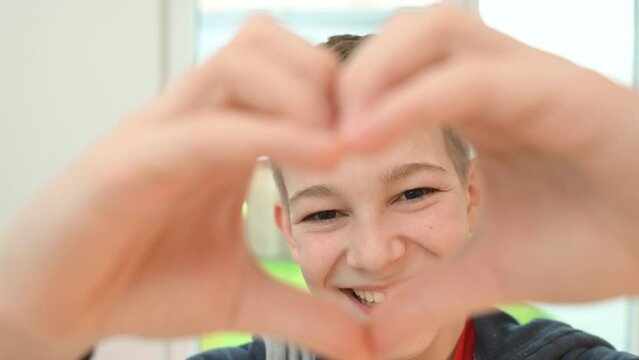Smiling happy teen boy showing heart shape with his fingers