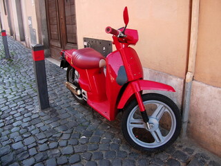 Red vintage scooter on an Italian street. Mobile urban transport. Paving stones on the road.