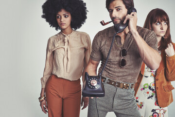 Too busy for chicks. Two attractive young hippies standing behind a handsome man using a retro telephone.