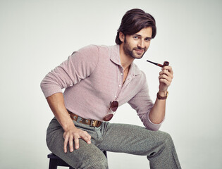 Groovy cool. A young man with 70s style sitting in the studio and smoking a pipe.