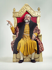 Fototapeta na wymiar Servants Come hither. Studio shot of a richly garbed king sitting on a throne.