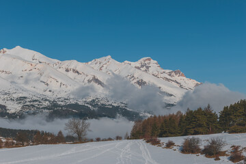 A picturesque landscape view of the snowcapped French Alps mountains with a hiking path in the snow on a cold winter day (La Joue du Loup, Devoluy)