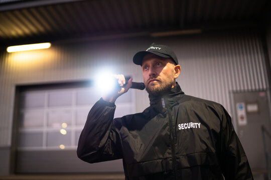 Security Guard Walking Building Perimeter With Flashlight