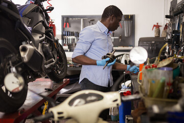 Confident worker examines a broken motorcycle part of the working area. High quality photo