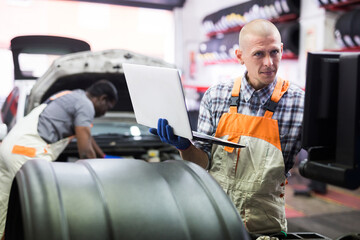 Mechanic man with laptop making car diagnostics at auto service