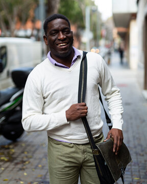 Positive African-american man smiling and looking in camera while walking through town streets.