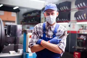 Obraz na płótnie Canvas Workman in protective mask standing near car at auto repair shop