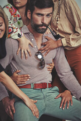The ladies love me. Studio shot of an attractive man in retro 70s wear surrounded and being touched by women.