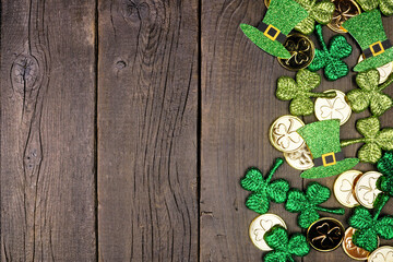 St Patricks Day side border against a dark wood background. Overhead view with gold coins, shamrocks and leprechaun hats. Copy space.