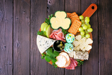 St Patricks Day theme charcuterie board against a wood background. Variety of cheese, meat, fruit and vegetable appetizers. Overhead view.