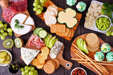 St Patricks Day theme charcuterie table scene against a wood background. Variety of cheese, meat,...