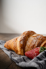 A butter Croisssant and strawberry on a napkin lined on a dark table with white wall.