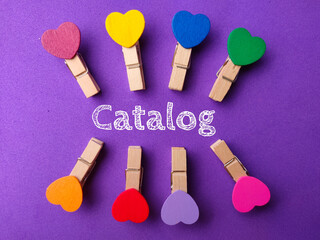 Top view colored wooden clips word Catalog on a purple background.