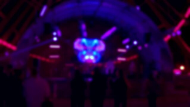Silhouettes of dancing people near a stage in nightclub: blurry background. Dancing at disco with neon rays of light and hologram. Concept of nightlife of young people in nightclubs.