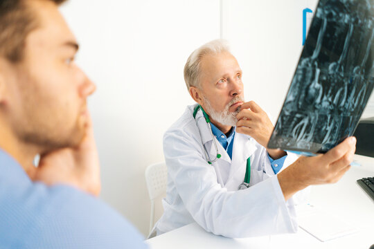 Close-up view from back of young male patient listening mature adult doctor explaining results of MRI scanning, giving professional consultation for treatment illness, explaining causes of disease.