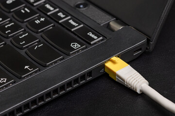 Computer ethernet network cable with yellow RJ-45 connector inserted into the black laptop on black...