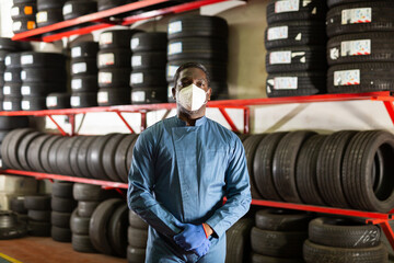 Fototapeta na wymiar Portrait of professional african american auto mechanic in face mask posing near car tires at auto service