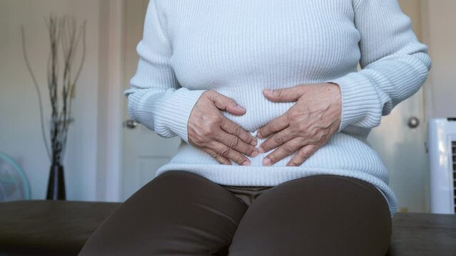 Elderly woman having painful stomach ache sitting on sofa,Female suffering from abdominal pain,Period cramps,Hands squeezing belly,Stomach pain,Menstruation