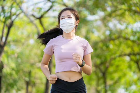 Runner woman wearing mask while running outdoor in covid-19 pandemic outbreak. Wear a face mask when you're running in an area where social distancing is hard to maintain.