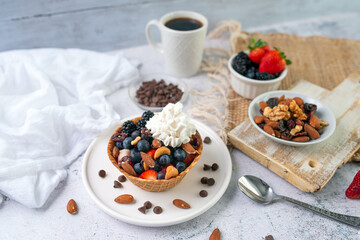 Fototapeta na wymiar Yogurt and fruit in a waffle bowl. Greek yogurt in ice cream waffle bowl with fruit and nuts, healthy diet friendly dessert. Fruity waffle bowl.