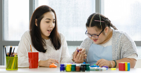 Asian lovely mother encouraging teaching cute daughter  painting acrylic colors on paper