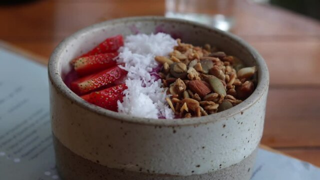 a bowl of strawberry smoothie bowl with coconut flakes, nuts, muesli. superfood healthy concept