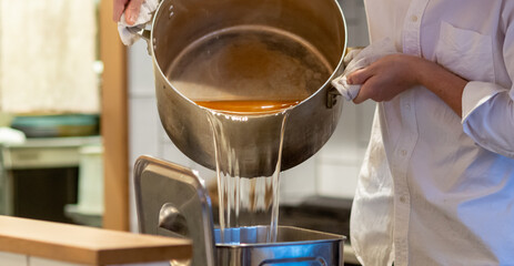 寸胴に入ったつゆ（出汁）を容器に移し替える料理人の手元