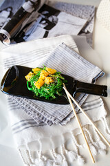 Japanese chuka salad with seaweed and orange. Served on a dark glass dish from a melted black bottle