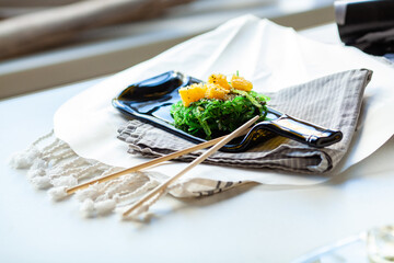 Japanese chuka salad with seaweed and orange. Served on a dark glass dish from a melted black bottle
