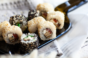 Japanese sushi food. Maki and rolls with tuna, salmon, shrimp, crab and avocado. Served on a dark glass dish from a melted black bottle