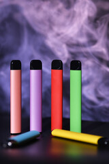 Set of colorful disposable electronic cigarettes on a black background with colour smoke. The...